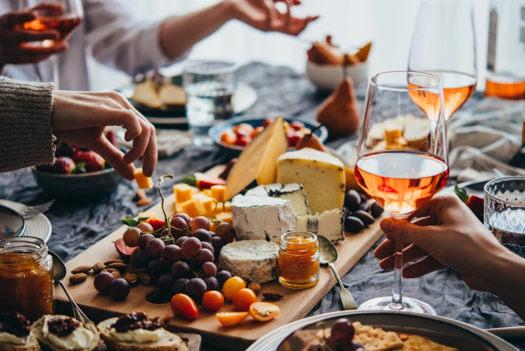 plateau de fromage et verres avec deux personnes en train de manger à la table